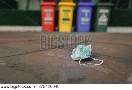 Used Medical Face Mask Discard On Pavement Floor On Blurred Recycle Bin Or Trash. Medical Waste Disp