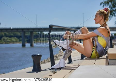 A stunner smiling summer closeup portrait of sexy young happy woman posing in a vintage roller skates, T-shirt, shorts posing on a road in city  hot summer day. Holidays and vacations.
