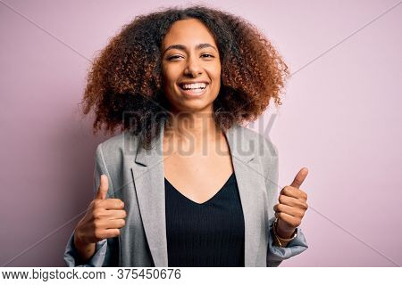 Young african american businesswoman with afro hair wearing elegant jacket success sign doing positive gesture with hand, thumbs up smiling and happy. Cheerful expression and winner gesture.