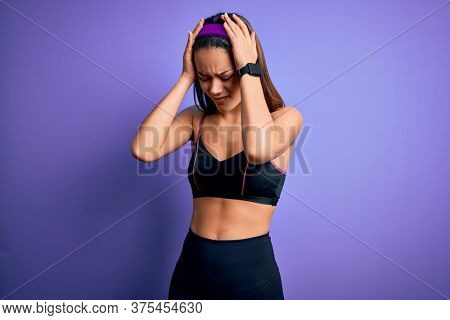 sporty girl doing sport wearing sportswear over isolated purple background suffering from headache desperate and stressed because pain and migraine. Hands on head.