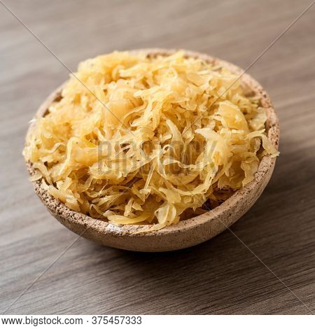 closeup of an earthenware bowl with cooked sauerkraut, german finely cut fermented cabbage, on a wooden surface