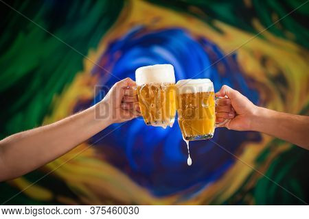 Two People Toasting With Mugs Full Of Draft Beer With Stylized Brazilian Flag Background