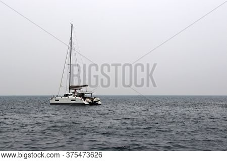 White Single-masted Yacht With A Deflated Sails In The Open Sea. Seascape In Storm Weather, Travel A