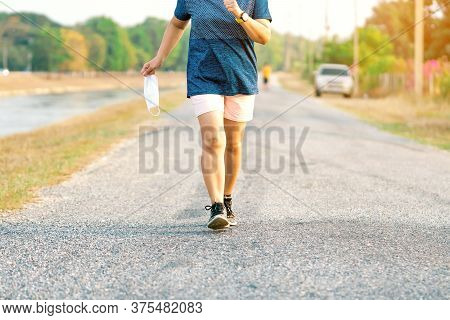 Sportive Woman Take Off Protective Mask While Jogging For Easier Breathing On Road Beside Irrigation