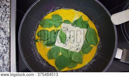 Spinach And Cheese Omelette Cooking In Frying Pan On Hob