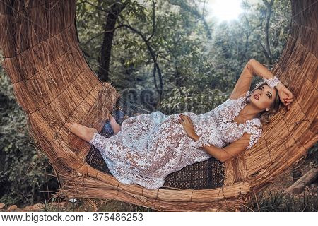 Beautiful Bride In Her Wedding Dress Posing For Photos On A Wooden Swing In The Tree.