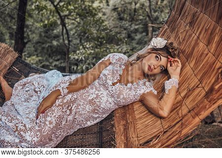 Beautiful Bride In Her Wedding Dress Posing For Photos On A Wooden Swing In The Tree.