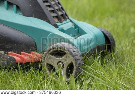 Dirty Lawn Mower Stands In Stems Of Green Grass. Garden Work Concept. Garden Equipment Maintenance C
