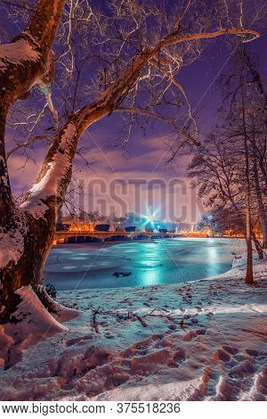 Frozen Lake In The Winter Shot During Night In A Park With A Bridge In The Background And Artificial