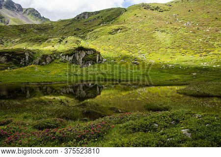 Small Alpine Lake Between The Green Fields And The Gray Granite Rock Of The Lagorai In The Trentino 