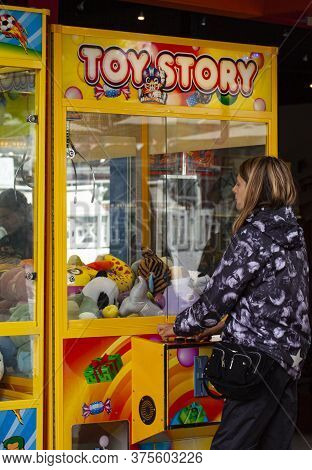 Girl Trying Her Luck At A Mr. Claw Crane Maschine. Classic Claw Grabber Game Machine Filled With Toy