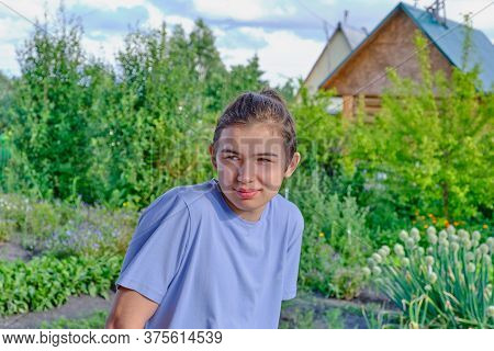Portrait Of A Shyly Smiling Teenager In A Blue T-shirt On The Background Of A Vegetable Garden And A