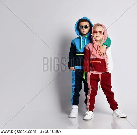 Elder Bro Hugging His Younger Sister. Stylish Sporty Kids In Colourful Tracksuits And Sunglasses. Ch