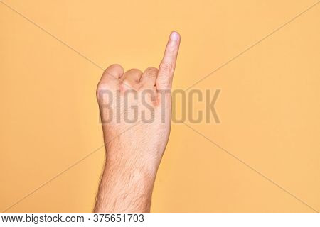 Hand of caucasian young man showing fingers over isolated yellow background showing little finger as pinky promise commitment, number one