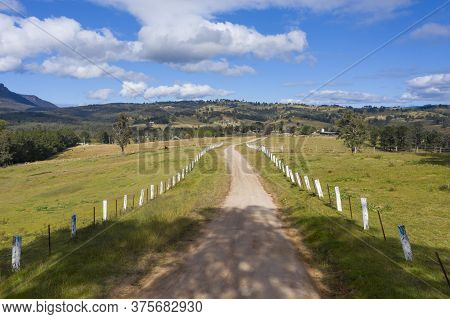 Aerial View Of A Dirt Road With White Fence Post Markers In A Green Agricultural Field
