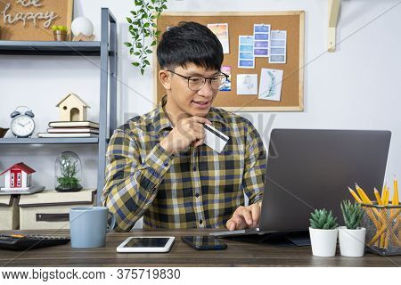 Asian Man Holding Credit Card To Online Shopping With Laptop Computer And Entering Security Code, In