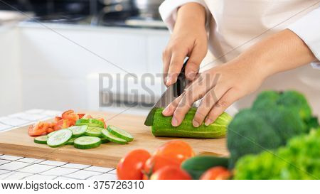 Young Asian Woman Is Preparing Healthy Food Vegetable Salad By Cutting Cucumber For Ingredients On C