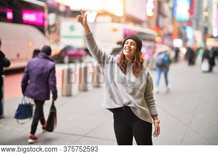 Young beautiful woman smiling happy and confident. Standing with smile on face and hand up calling cab at the city