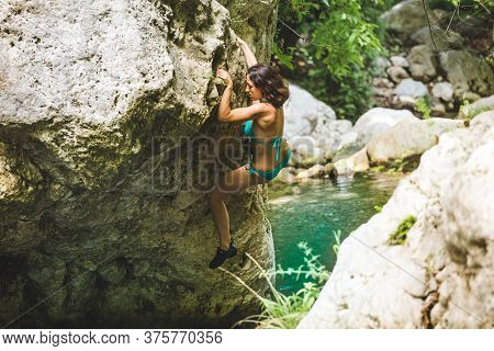 A Woman In A Swimsuit Climbs A Cliff Above The Water, Climbing Over A Mountain River, Bouldering In 
