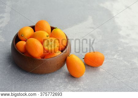 Kumquat Fruits In Wooden Bowl On Light Stony Background. Healthy Vegetarian Food. Kumquat Fruit Cut 