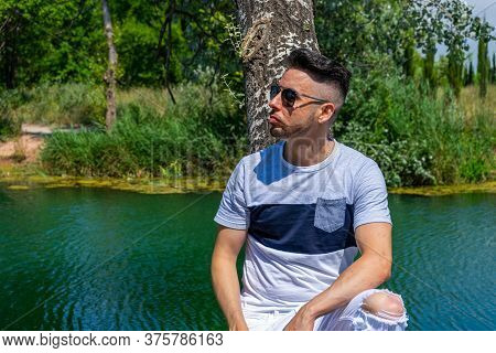 Young Man In White Pants And Modern Styling Posing In The Freshwater Pond Of Clot De La Mare De Deu 