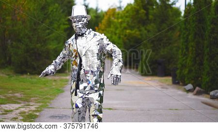 Elegant Man In Mirror Suit And Hat Is Dancing In The Street. Beautiful Green Trees Are On The Backgr