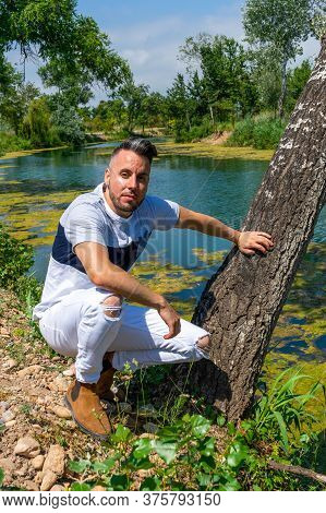 Young Man In White Pants And Modern Styling Posing In The Freshwater Pond Of Clot De La Mare De Deu 