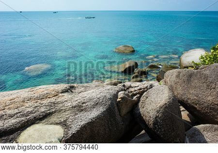 Tropical island coast with turquoise clear water, rocky bottom, boulders, boat in open sea. Koh Tao island popular destination for travel holidays in Thailand