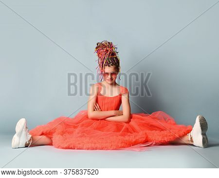 Kid Girl With Colorful Dreadlocks In Bright Coral Big Dress, Sneakers, Sunglasses Is Sitting On Floo