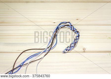 Shot Of A Half Finished Braided Leather Bracelet Made From Black, Blue And White Leather Cords