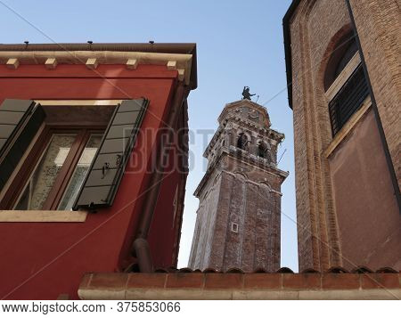 The Bell Tower Of Santa Maria Dei Carmini Through A Gap Between Buildings, Venice, Italy