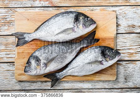 Raw Dorada Or Sea Bream On Choppong Board Over White Wood Table Top View.