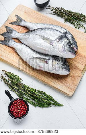 Dorado Or Seabream Fish Set On Chopping Board With Herbs For Grill Uncooked  On White Textured Backg