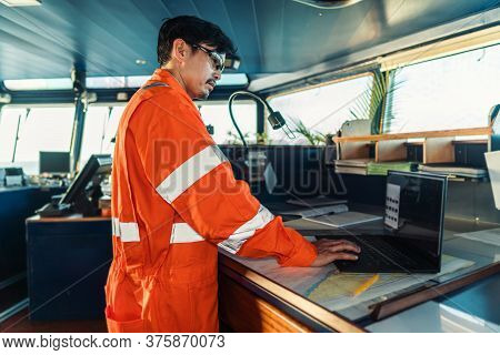 Filipino Deck Officer On Bridge Of Vessel Or Ship. He Is Using Laptop, Electronic Paperwork At Sea