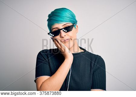 Young woman with blue fashion hair wearing thug life sunglasses over white background thinking looking tired and bored with depression problems with crossed arms.