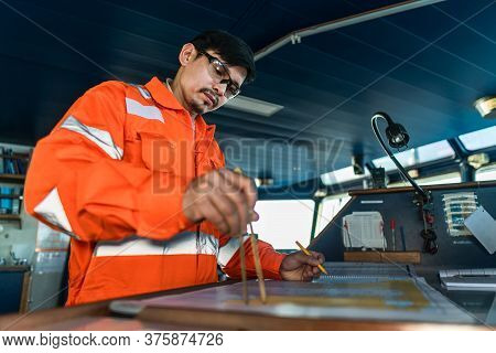 Filipino Deck Officer On Bridge Of Vessel Or Ship. He Is Plotting Position On Chart