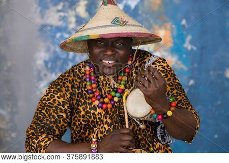 African Man In Traditional Clothes And Fulani Hat Playing On Talking Drum