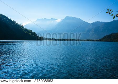 Trees Are Reflected On Lake Levico With The Mountains In The Background In Trento, Italy