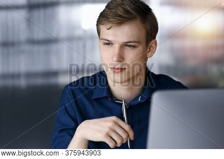 Young Blond Businessman Thinking About Strategy At His Working Place With Computer In A Darkened Off