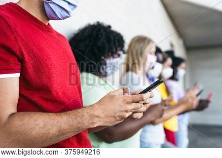 Young People Wearing Face Mask Using Mobile Smartphone Outdoor - Multiracial Friends Having Fun With