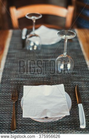 Light Wooden Table Setting: White Plates, Rustic Dark Table Cloth With Salami, Cheese, Vine, And Ham