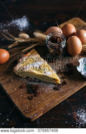 Traditional Italian Cake With Ricotta Cheese And Raisin, Eggs, Jar And Powdered Sugar On Wooden Back