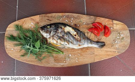 Dorado Fish Was Cooked With Lemon Over An Open Fire And Lies On A Wooden Board With Herbs And Slices