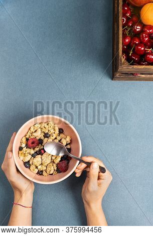 Girl Eating Breakfast And Muesli With Wooden Spoon In A Bowl With Milk With Seasonal Fruits