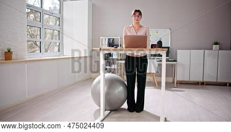 Woman Using Adjustable Height Standing Desk In Office For Good Posture