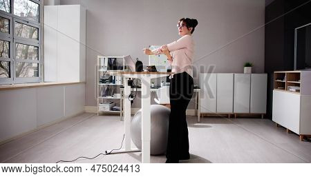 Woman Using Adjustable Height Standing Desk In Office For Good Posture