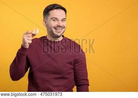 Happy Man Holding Tasty Fortune Cookie With Prediction On Orange Background. Space For Text