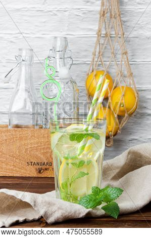 Lemonade With Mint In Glass, Lemons In Grid Bag And Bottles In Crate On Wooden Table. Side View Of F