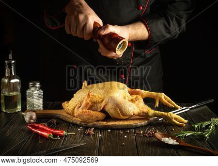 Professional Chef Prepares Raw Rooster In The Kitchen. The Cook Adds Black Pepper To The Cock Before