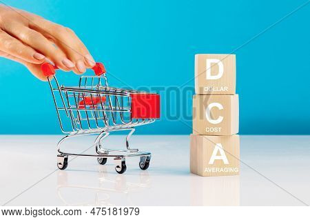 The Text Dca Is Written On Wooden Cubes And Woman's Hand Pushingn Empty Shopping Cart In Studio On B